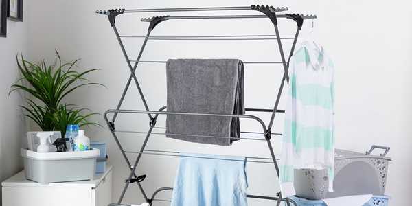 A 3 tier extra wide indoor clothes airer in black placed in a unitlity room next to 3 laundry baskets. 